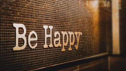 Be happy signage on black tiled wall, positive motivational message interior decor.