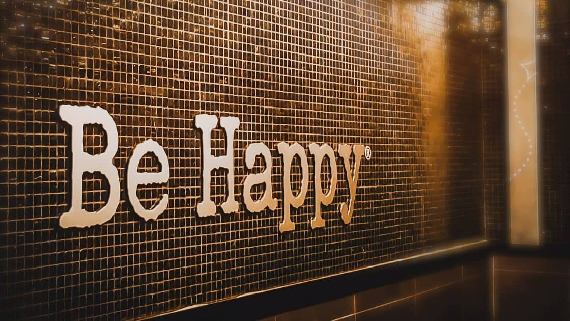 Be happy signage on black tiled wall, positive motivational message interior decor.