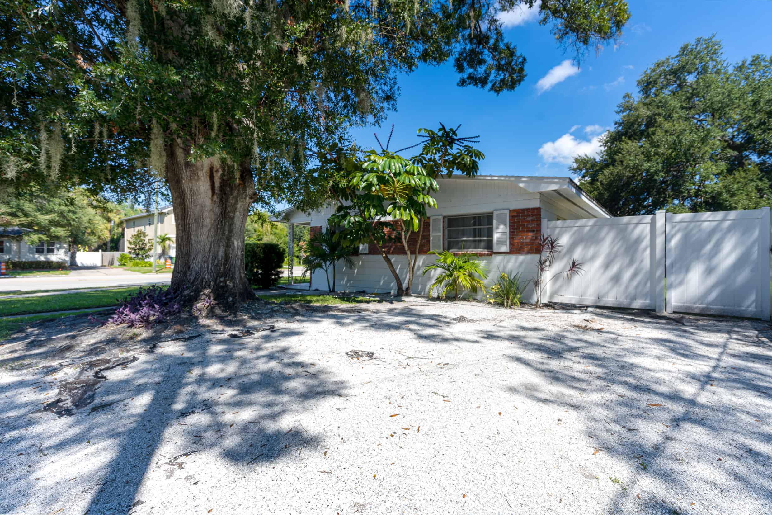 Lush front yard of a charming Florida home with mature trees and tropical landscaping.