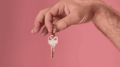 Key held by hand on pink background, symbolizing homeownership and real estate in Tampa.