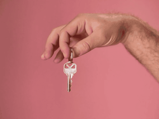 Key held by hand on pink background, symbolizing homeownership and real estate in Tampa.