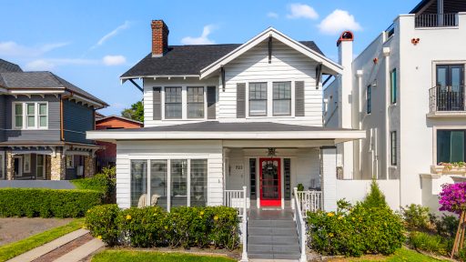 White vintage-style house with a red front door, landscaped yard, and neighboring homes in Tampa, Florida.