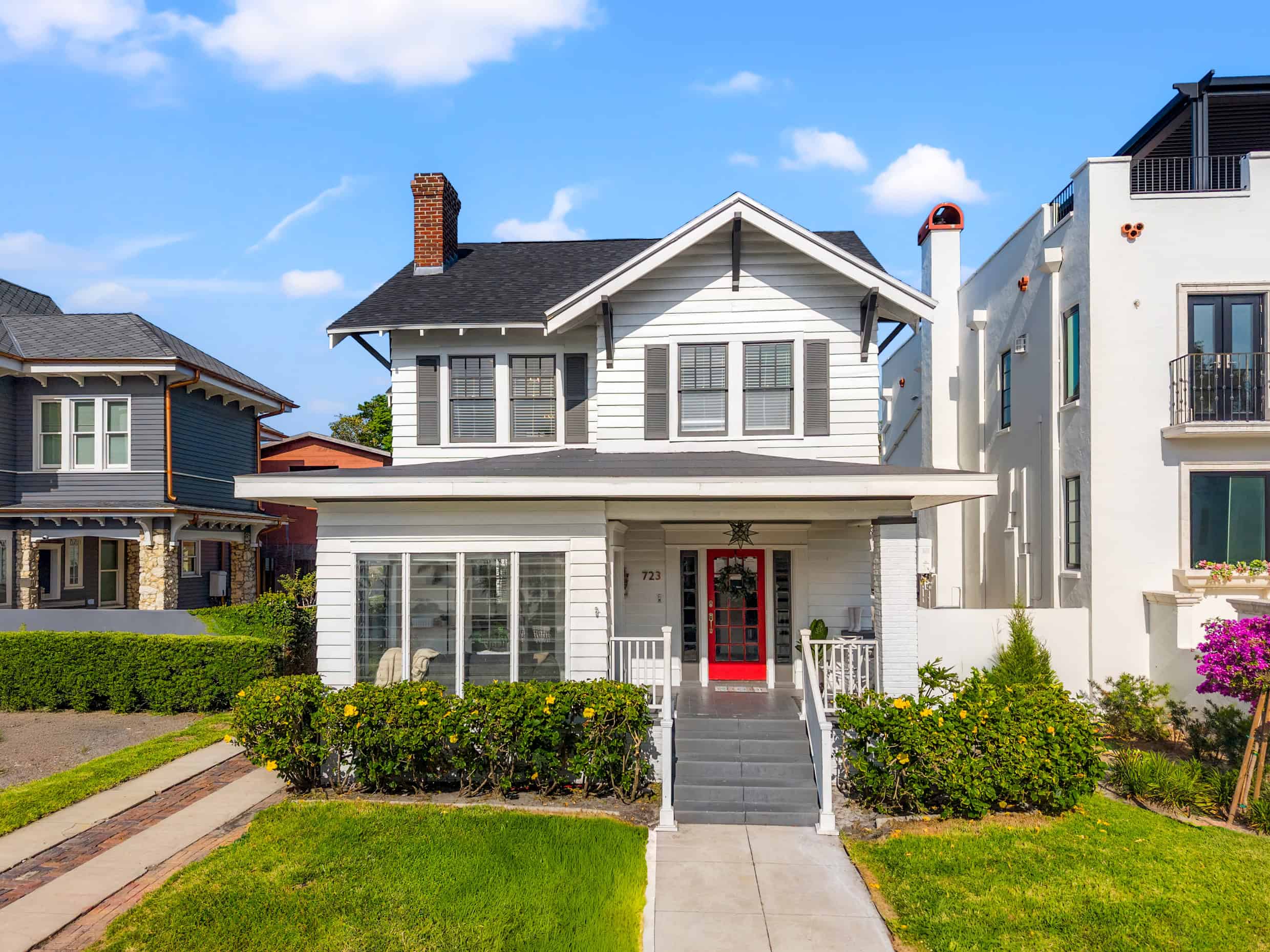 White vintage-style house with a red front door, landscaped yard, and neighboring homes in Tampa, Florida.