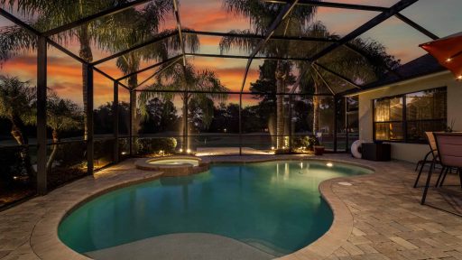 Spacious screened-in pool enclosure with a heated pool and hot tub at sunset.