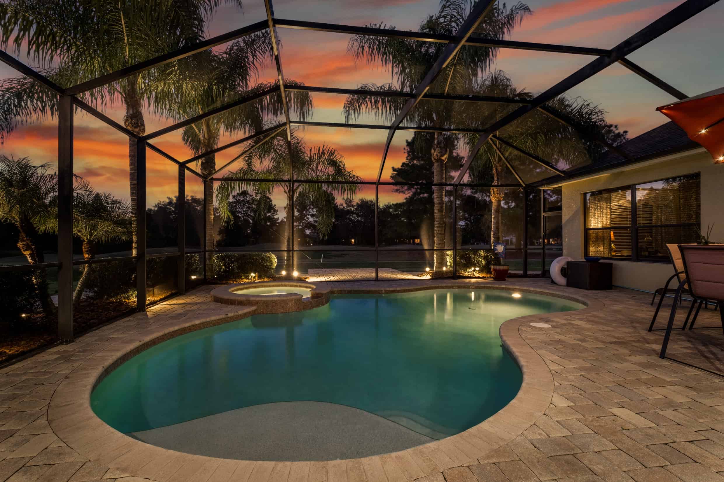 Spacious screened-in pool enclosure with a heated pool and hot tub at sunset.