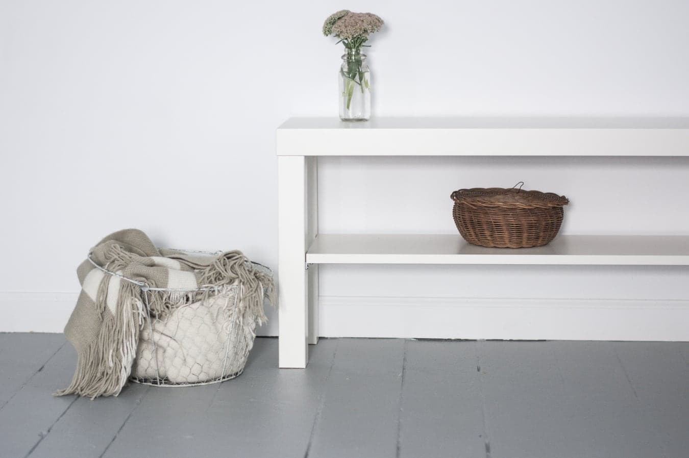 Cozy living room decor with a white bench, wicker basket, blanket storage, and fresh flowers in a glass vase.